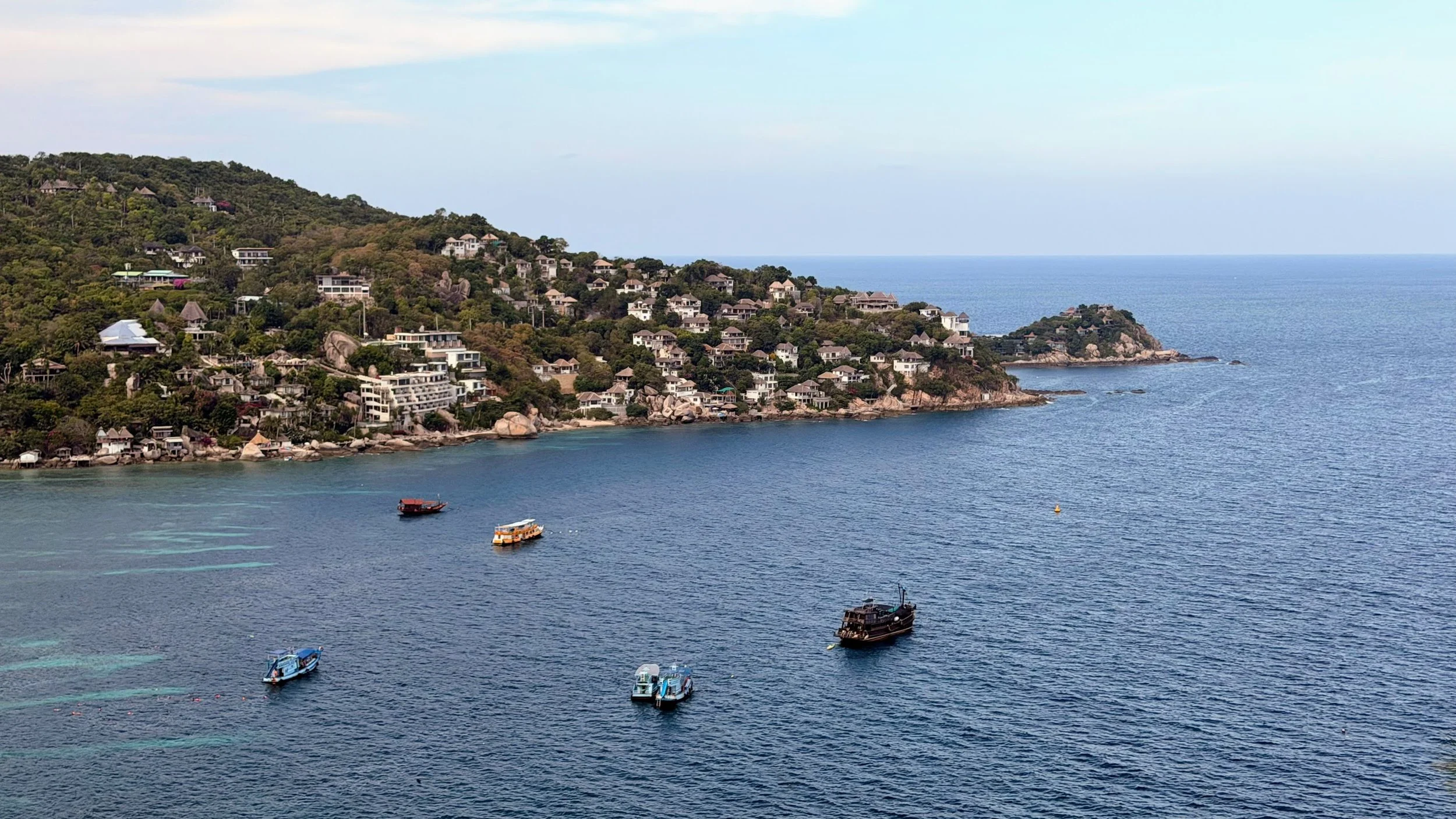 Taken from a viewpoint on a hilltop, a peninsula of Koh Tao island in Thailand is dotted with homes, villas and hotel, with several snorkeling boats in the bay.