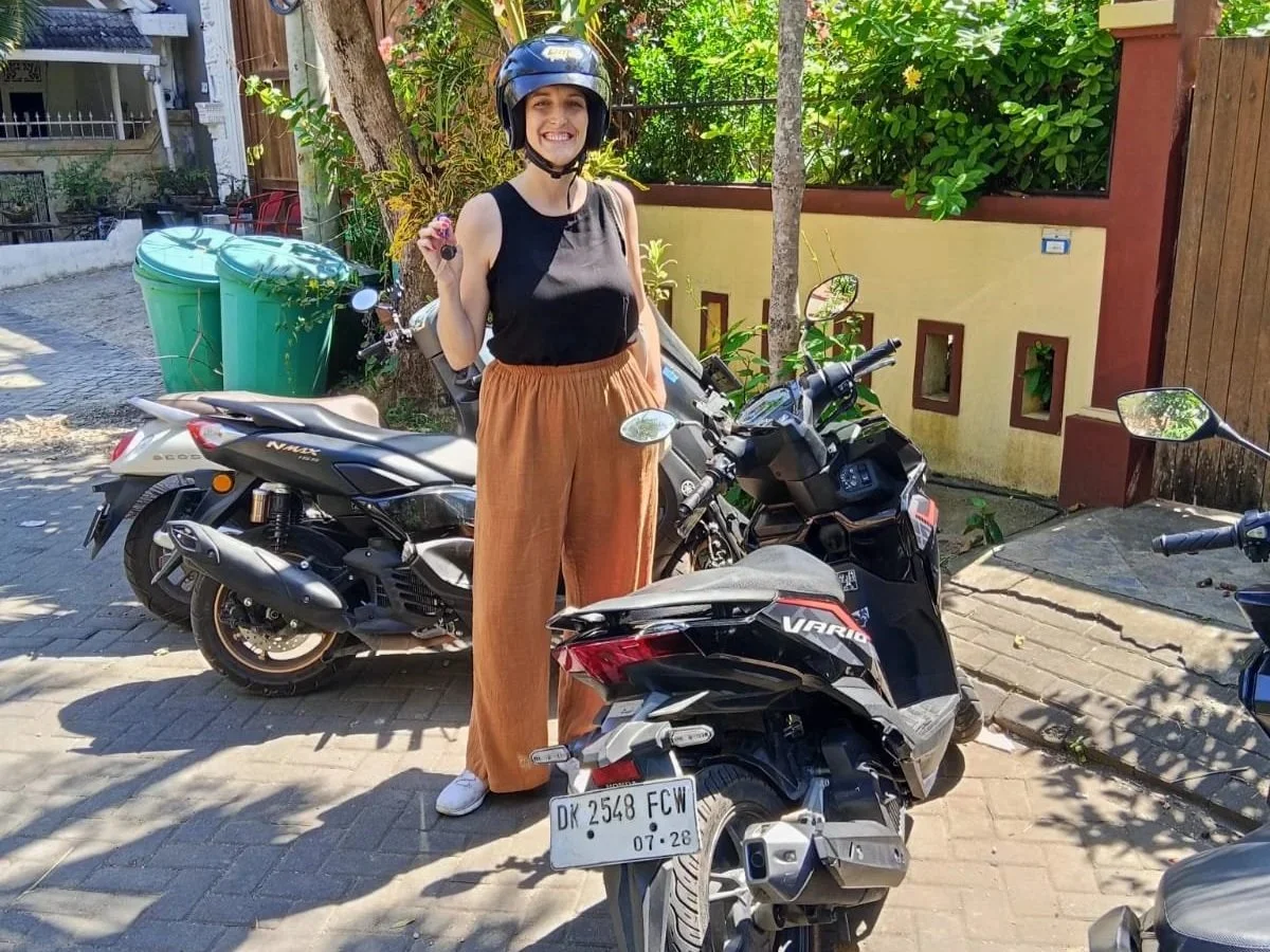 Lynne stand next to her first rental scooter, a Honda Vario, holding the keys and wearing a helmet in Bali, Indonesia