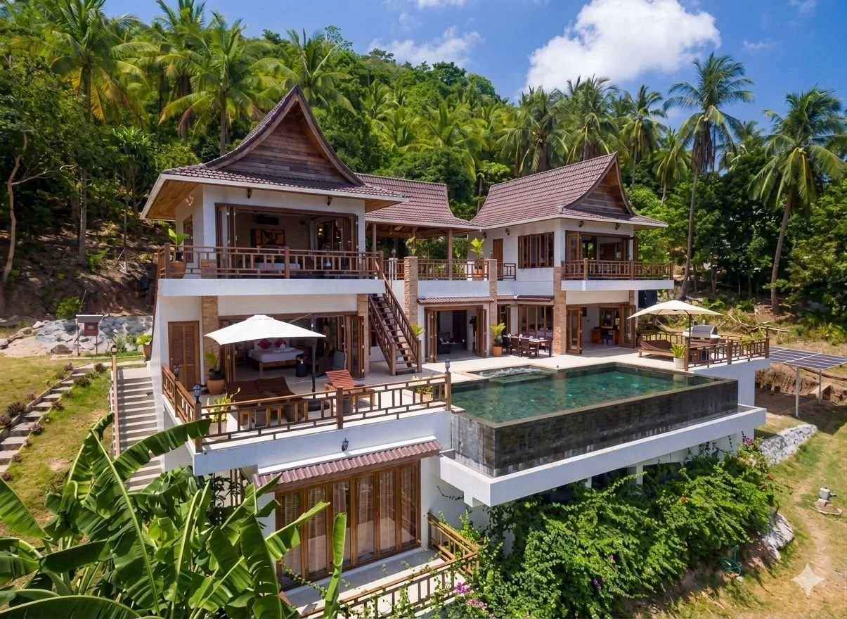 A wooden two story villa is perched on a hill, with an infinity pool over the edge and a palm tree forest background in Koh Tao, Thailand.