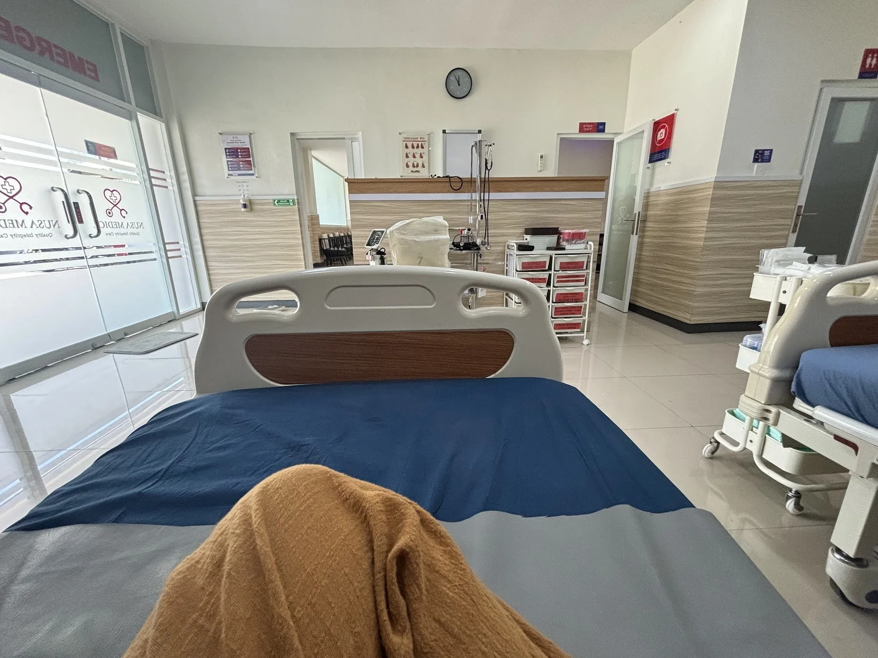 View from a hospital bed in a clinic in Uluwatu, Bali, with a clean clinic and medical supplies in the distance.