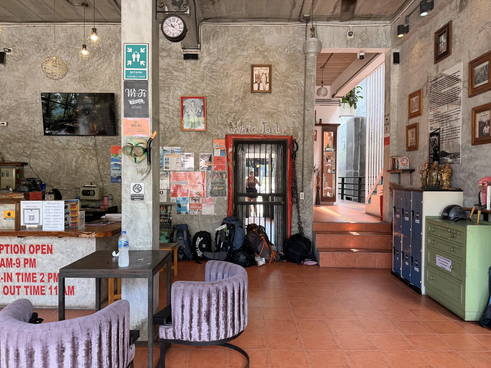 The lobby of White Jail hostel in Koh Tao, Thailand. Industrial in style with concrete walls and orange and purple accents, a reception area, lockers and cafe-style seating.
