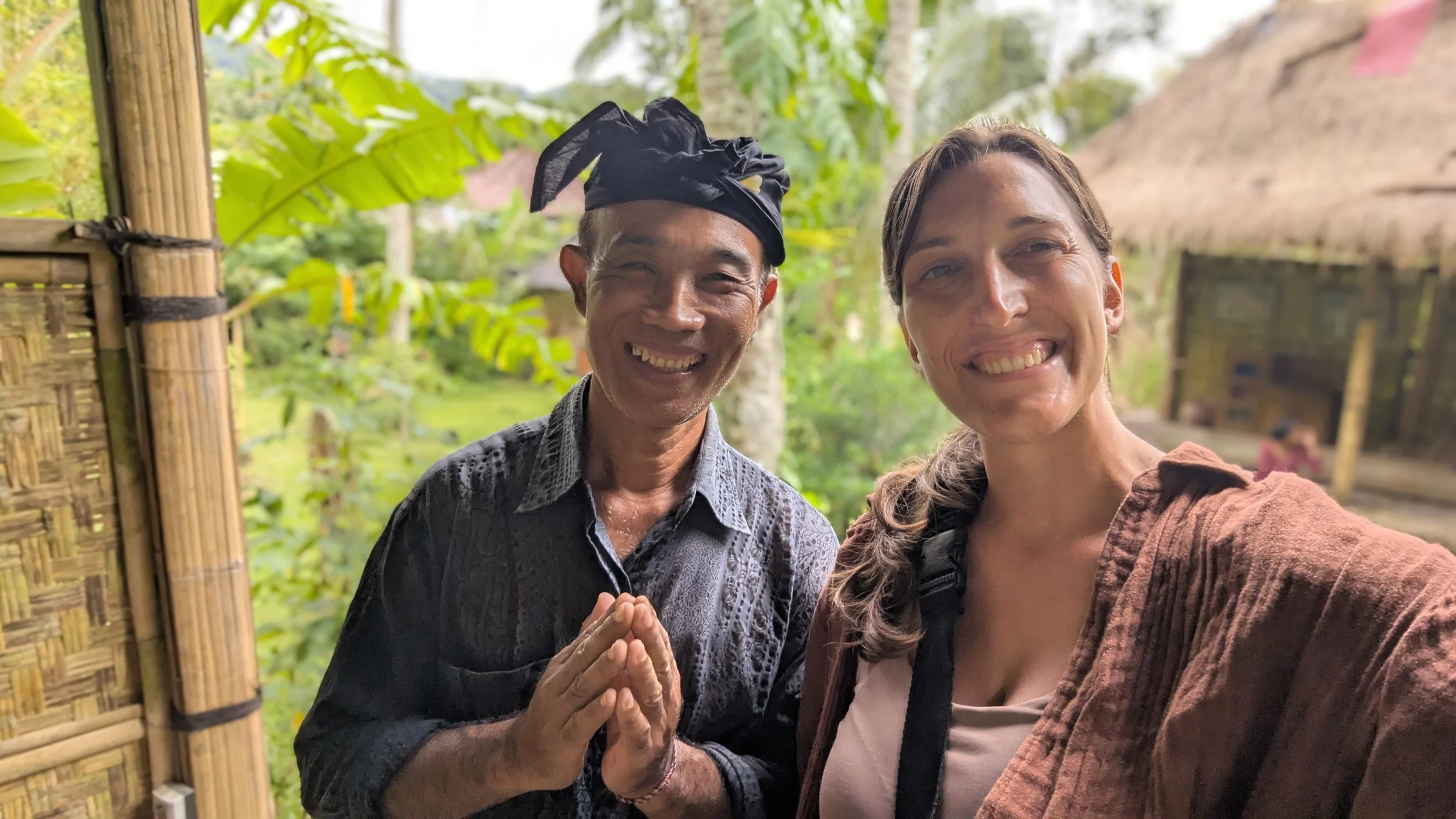 Lynne and Wayan from Samsara Living Museum in Karangasem, Bali, with a bamboo structure behind them and green palms