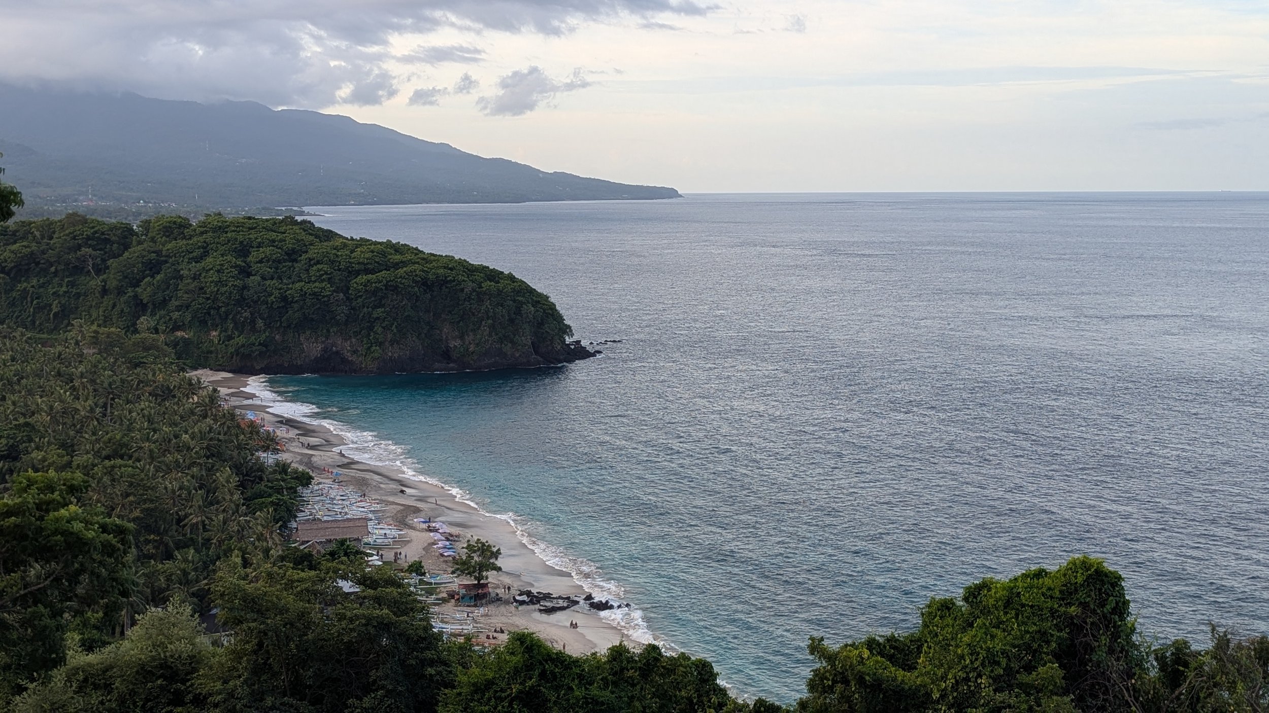 Amed's coast pictured from high up, with dense green forests and a beach peeking into the sea