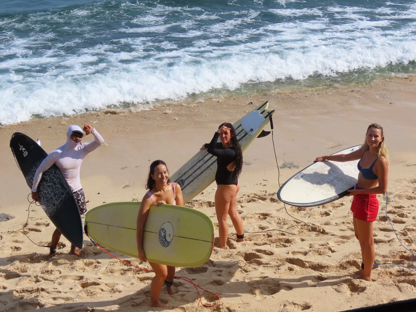 A surf instructor and 3 students stand on the beach each holding a board, about to head into the water
