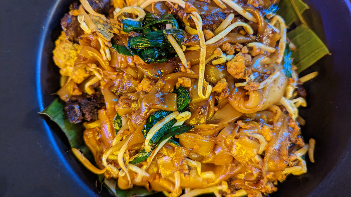 A close up on a plate of char kwey teo, a famous noodle dish in Malaysia, with flat noodles, bean sprouts, greens, sauce and more