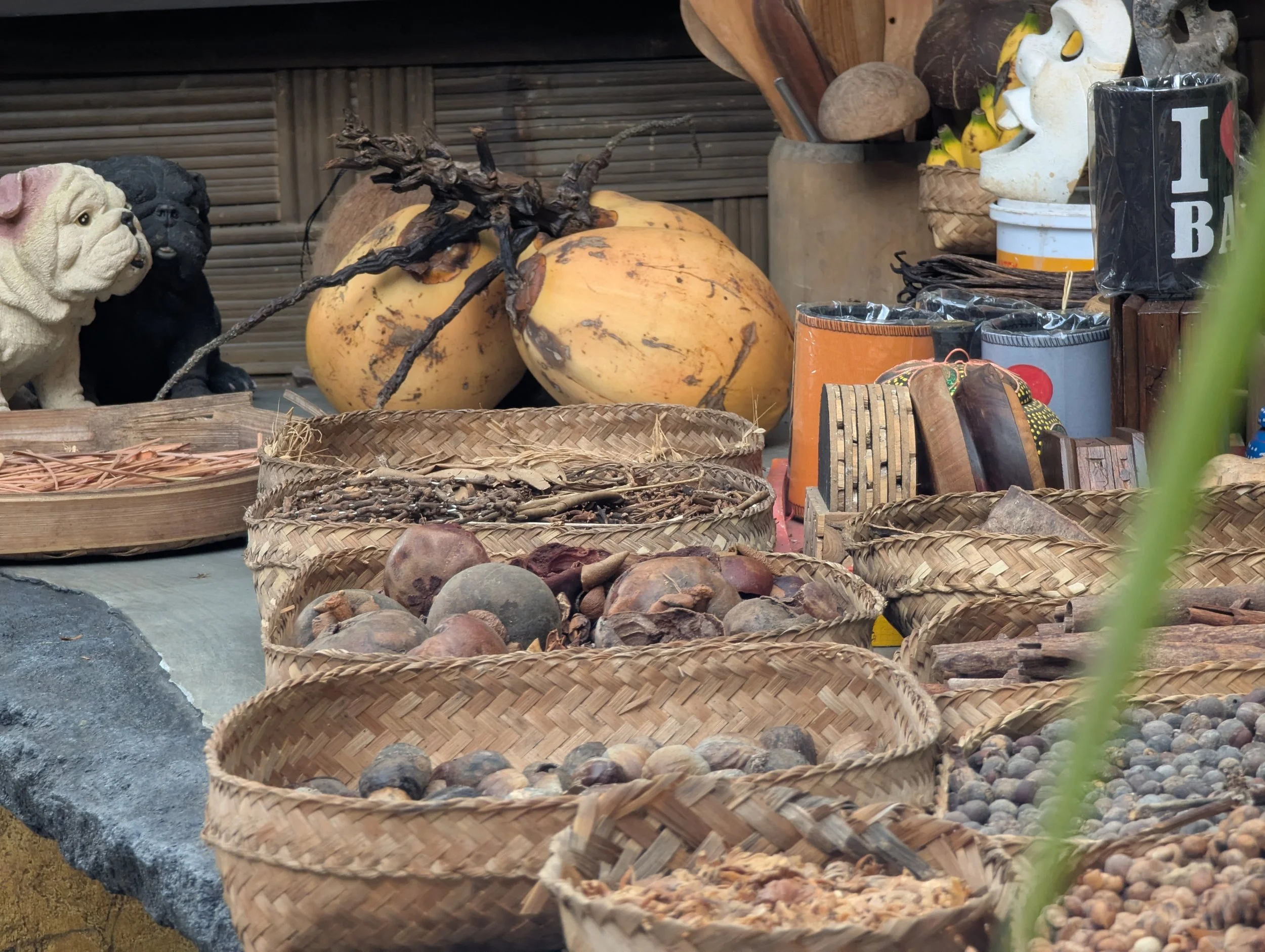 A table with woven baskets full of fresh spices, as well as coconuts and souvenir trinkets for sale on the waterfall trek path in Munduk, Bali