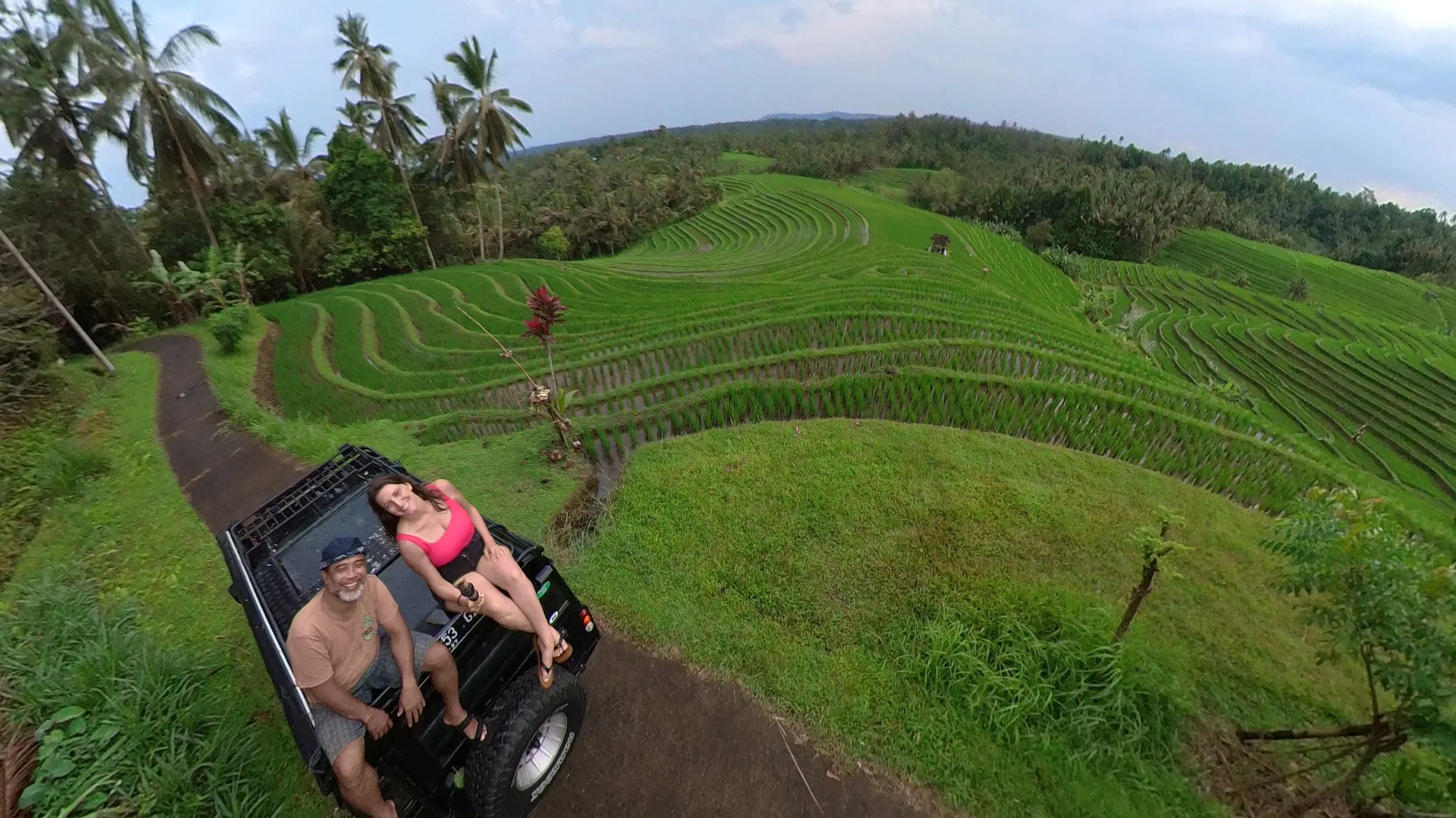 A woman tourist and a local guide sit on top of a black land rover  in a rolling green ricefield