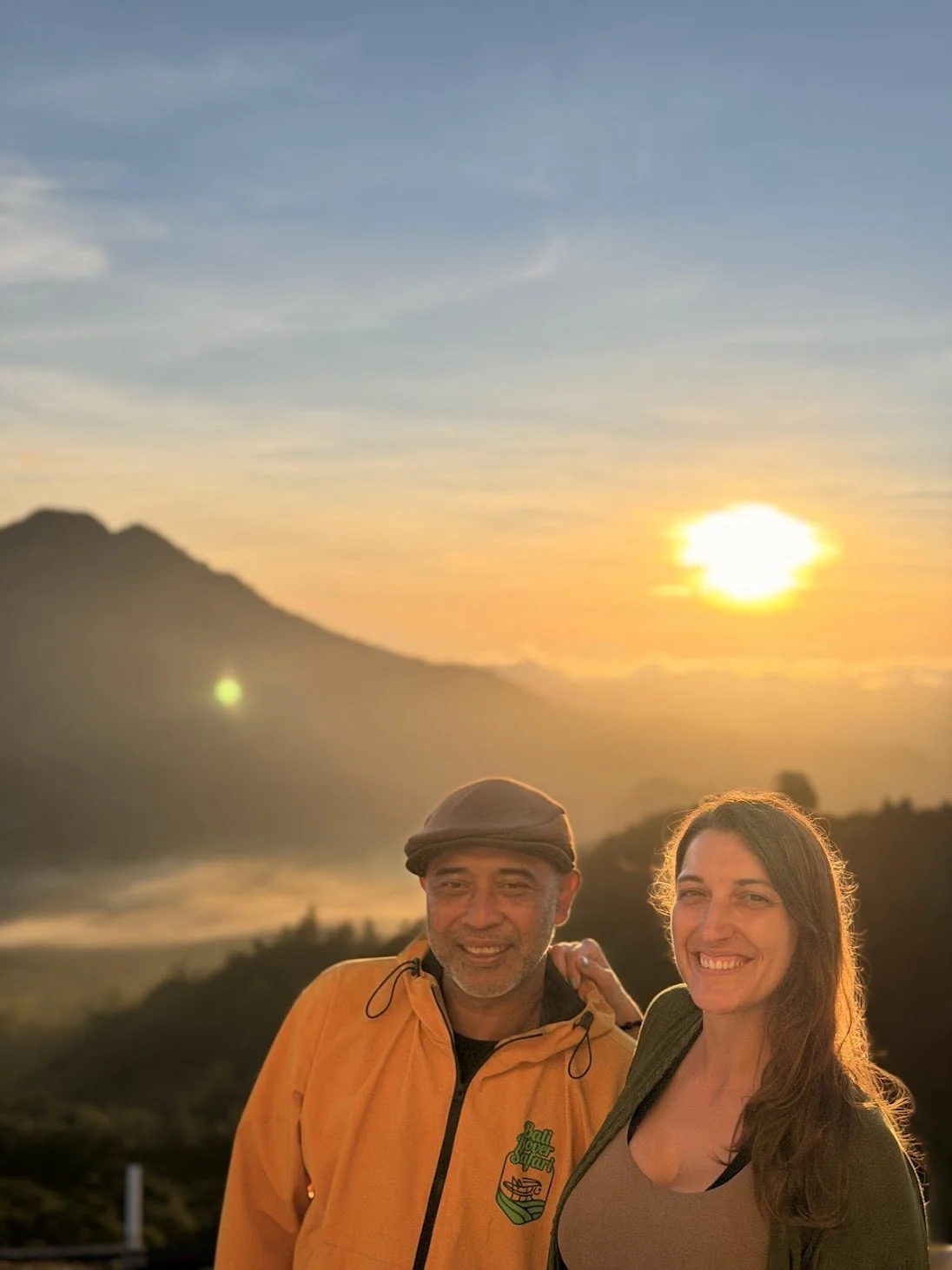 Lynne and Agung pose for a photo during an orange and yellow sunrise in front of Mount Batur volcano