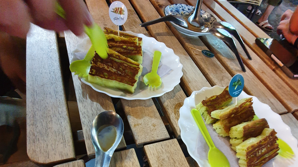 Two plates of pandan cake sit on a wooden table in Jalan Alor, Kuala Lumpur