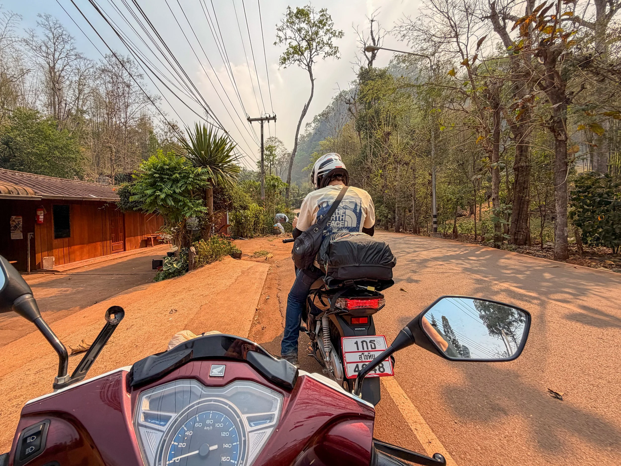 POV from a scooter on the Mae Hong Son Loop in Thailand, with another rider pulled over in front of her, with a backpack strapped to the back of his bike.