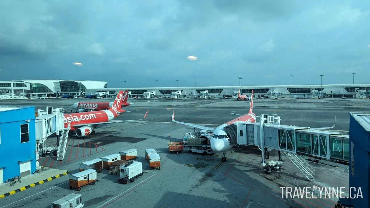 Three Air Asia planes wait on the tarmac with jet bridges and stairs leading up to them at KLIA