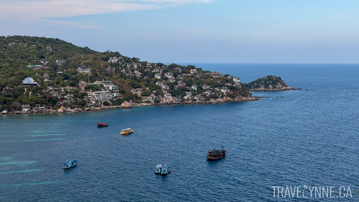 A peninsula stretches over the blue sea in Koh Tao, with 5 boats in the bay for snorkeling trips.