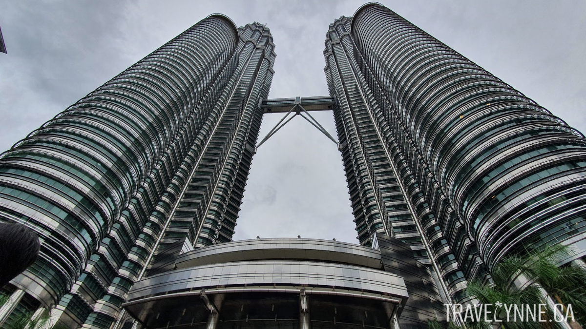 The Petronas Towers seen from their base, looking up to a cloudy sky, with a connecting walking bridge between them