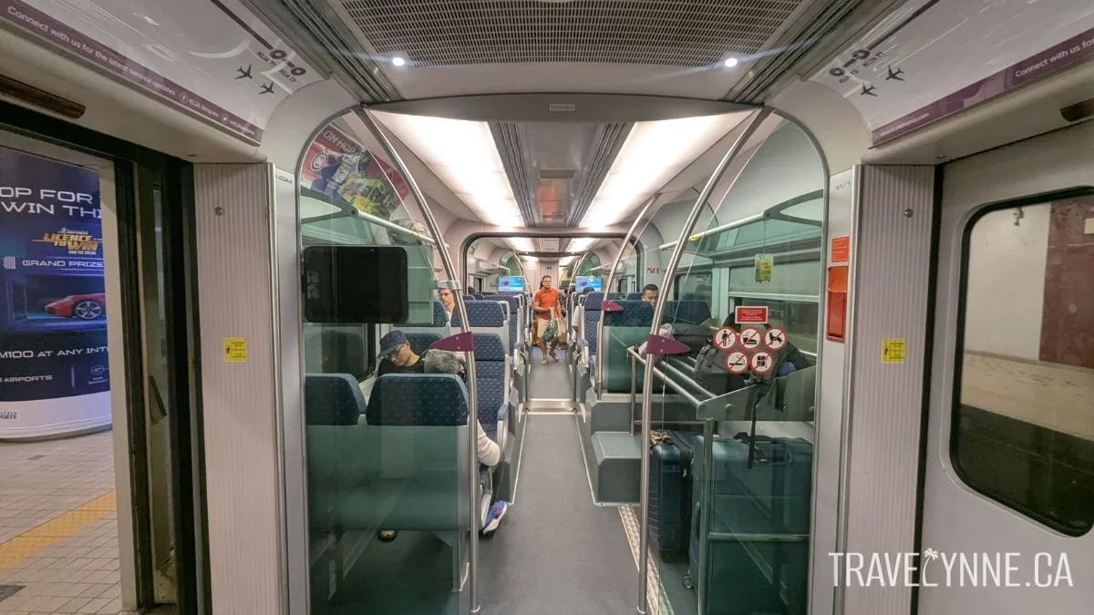 The inside of a KLIA Ekspres (airport) train, with seats in groups of 4 facing each other, some customers seated, and a rack with a few luggage items on it