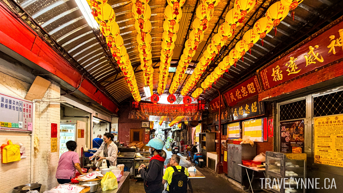 A unique 55 year old breakfast stall in Taipei, located inside a temple entrance, with red Chinese signage on the side walls and yellow lanterns hanging overhead