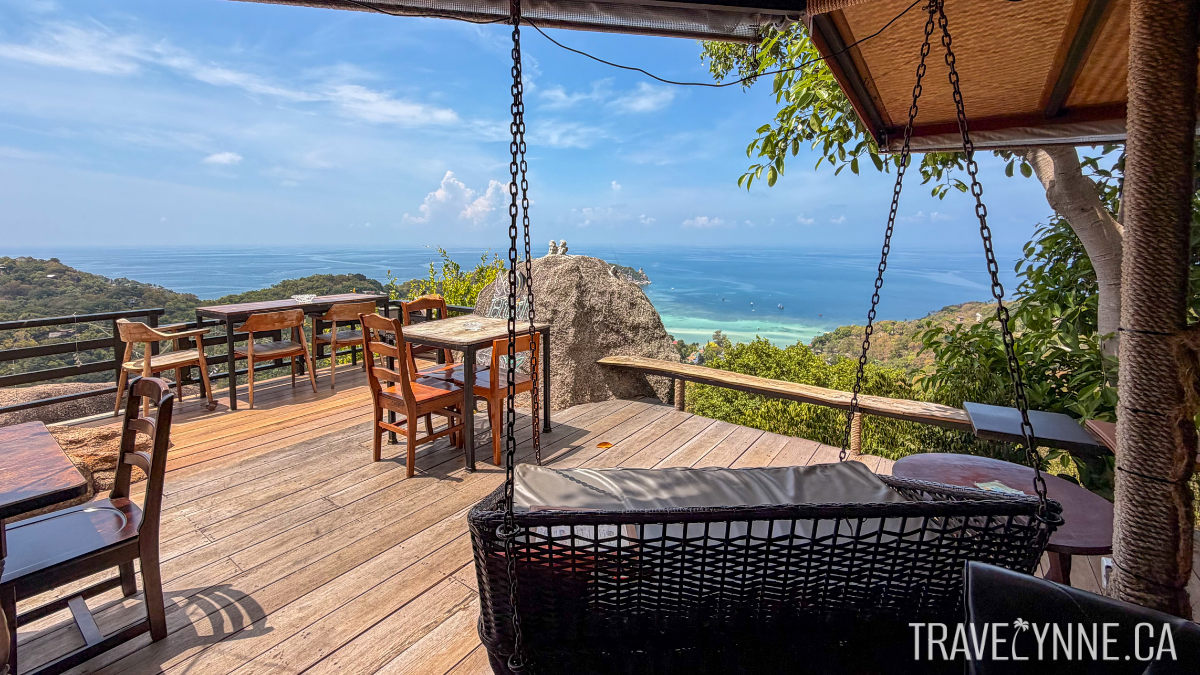 The patio of High the Moon restaurant in Koh Tao sits on a hill overlooking the blue sea, with table seating and a swing.