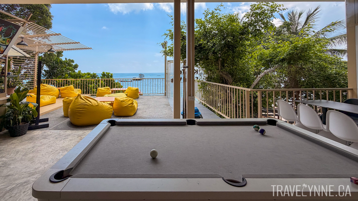 The upper level of open-air Foodville in Sairee Beach, with a pool table, trees, bean bags and floor tables, and the ocean in clear view.