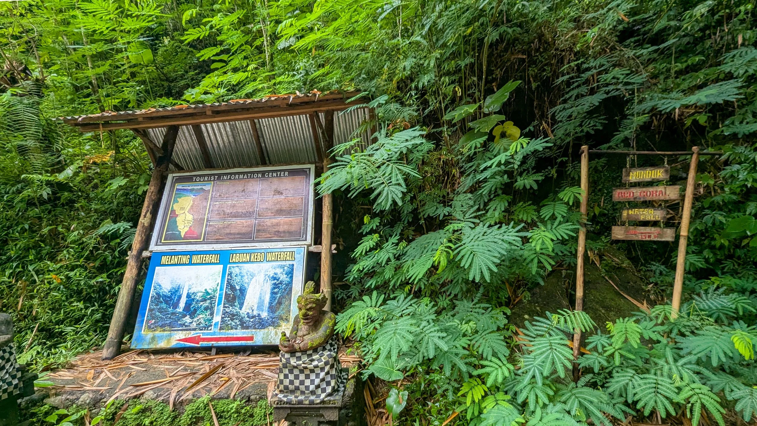Signage in a forest shows maps and directions towards Melanting Waterfall, Labuan Kebo Waterfall and Red Coral Waterfall