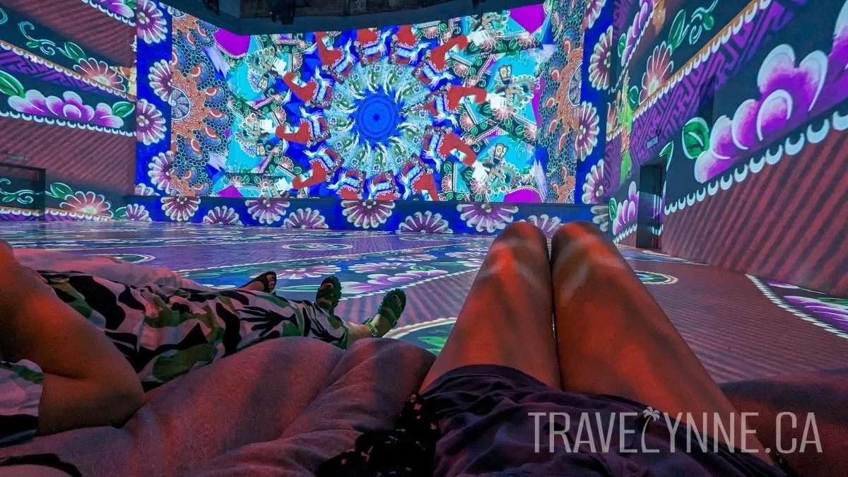 Legs of two women are seen relaxed on bean bags on the floor of an immersive art exhibit in REXKL.