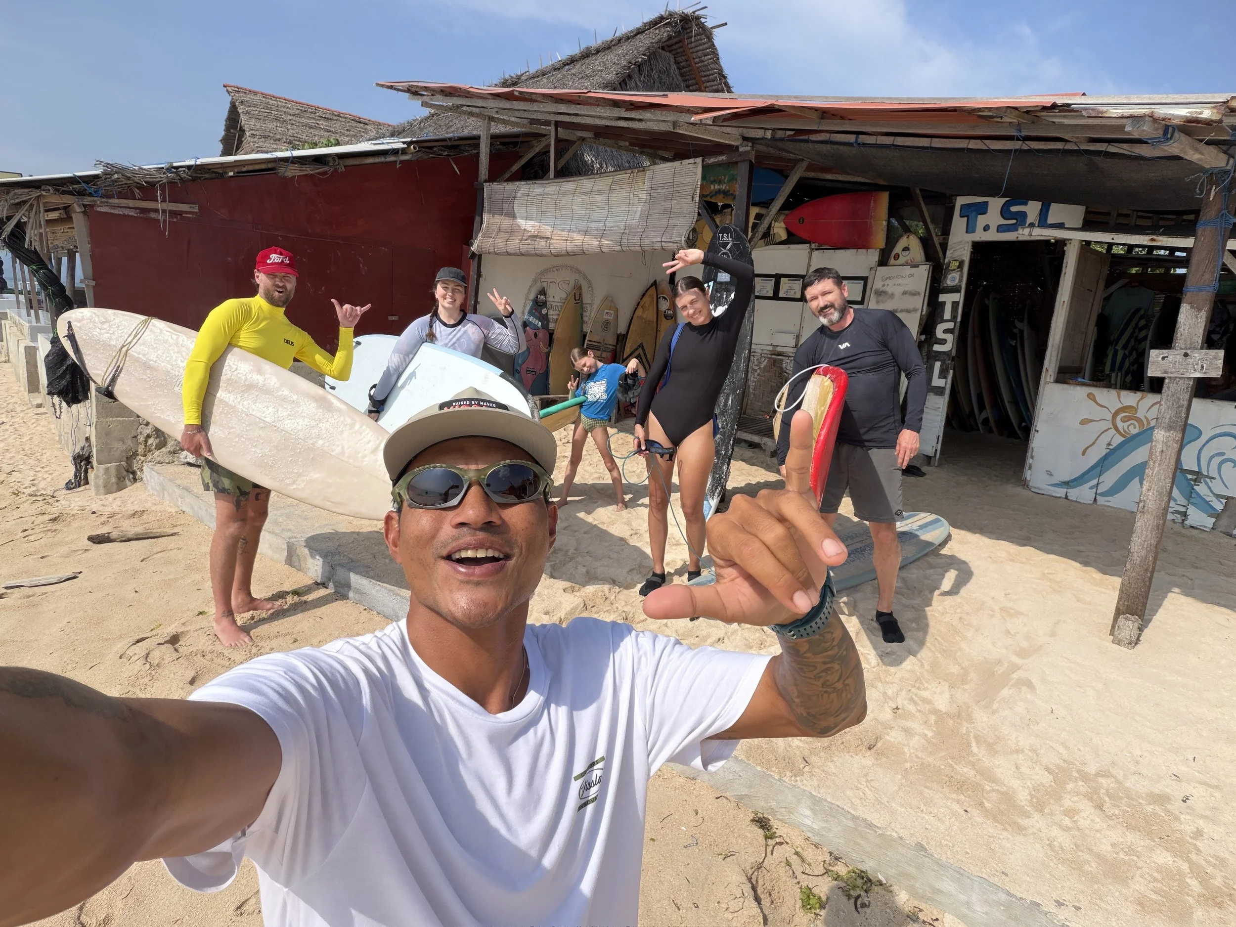 A surf instructor in Lembongan takes a selfie at the beach with 4 adult and 1 child surf student behind him