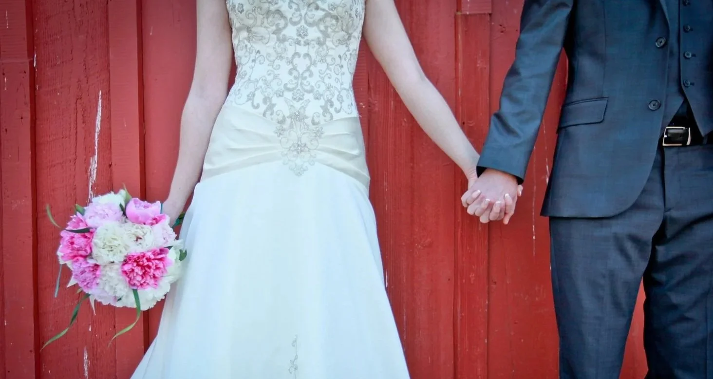 A bride and groom hold hands while standing in front of a red barn.