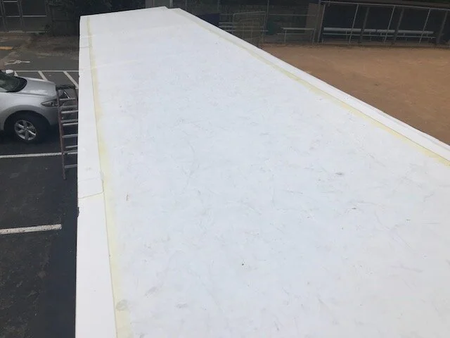 Top view of a flat, white rooftop with some dirt marks, adjacent to a parking lot and a dirt field.