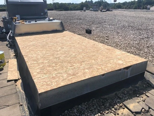 Flat rooftop with a large piece of plywood and some construction materials on the side, under a clear sky.
