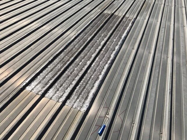 Metal roof with a central patch of damaged or worn roofing material and a screwdriver laying on the surface.