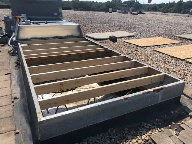 A rooftop HVAC unit with wooden framing for a new installation on a gravel-covered rooftop.