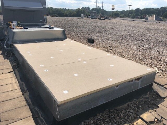 Flat rooftop with a large gray HVAC unit and a view of a parking lot with cars, trees, and a McDonald's sign in the background.
