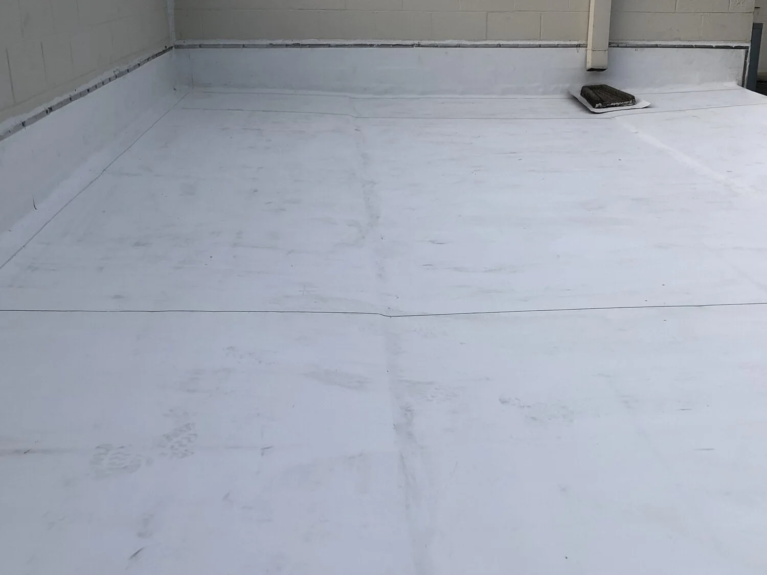 Flat roof surface with white waterproofing membrane and a vent pipe towards the back right corner.