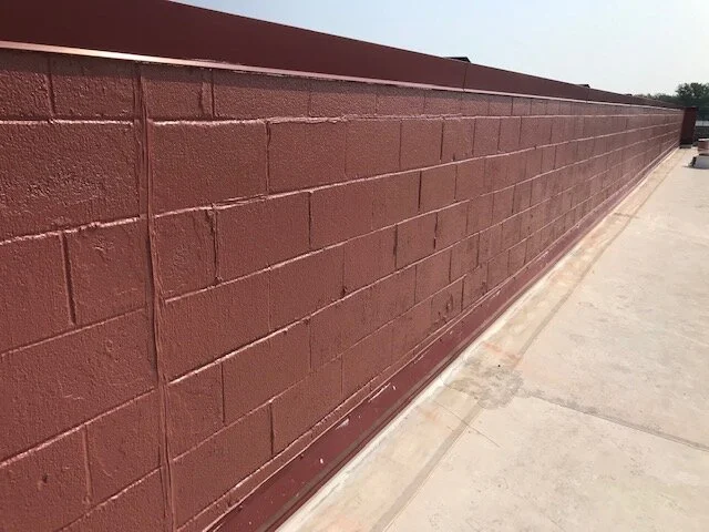 Long brick wall painted in reddish-brown color along a sidewalk.