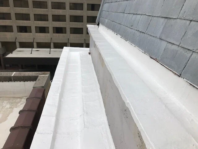 Roof edge with a white waterproof membrane in an urban setting with building rooftops in the background.