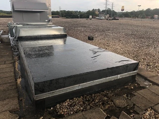 Flat rooftop with water on its surface, surrounded by stone pavers, with a parking lot and McDonald's in the background.