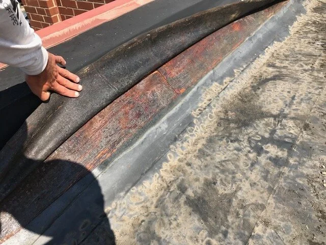 Close-up of a roofing surface with a person’s hand holding down a section of roofing material, which appears weathered and aged.
