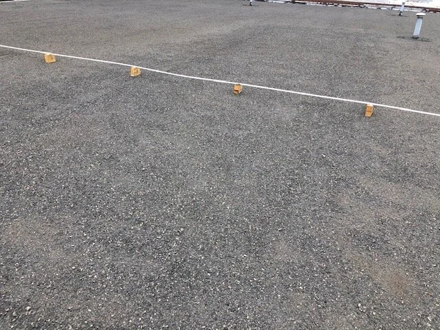 A gravel parking lot with a white rope barrier and small wooden blocks supporting it.