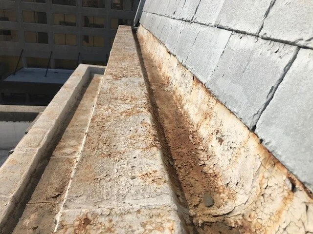 Close-up of a building's rooftop with a rusted edge and layered materials, including brick and concrete.