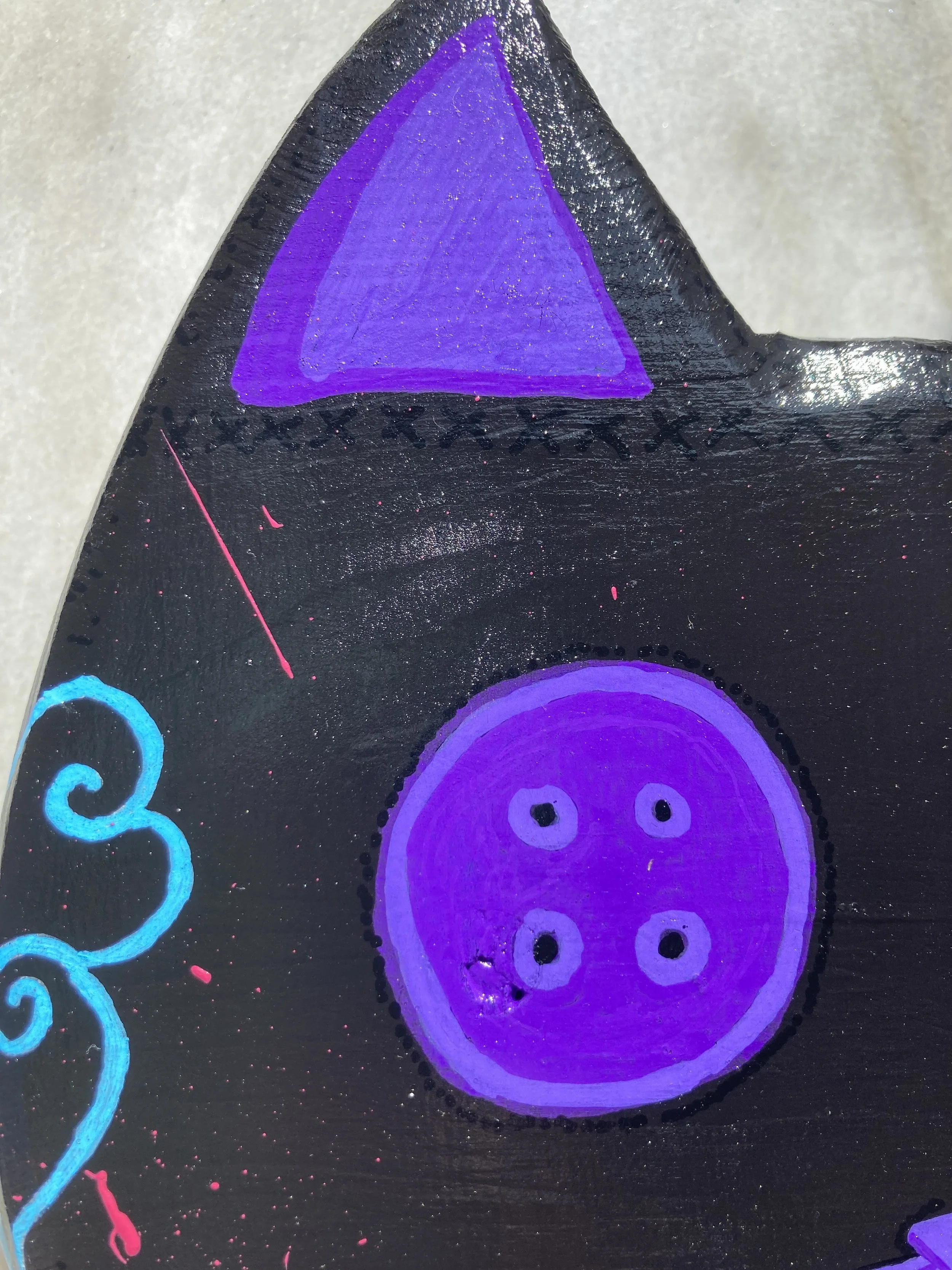 Painted wooden cat head, focused on purple button eye detail.