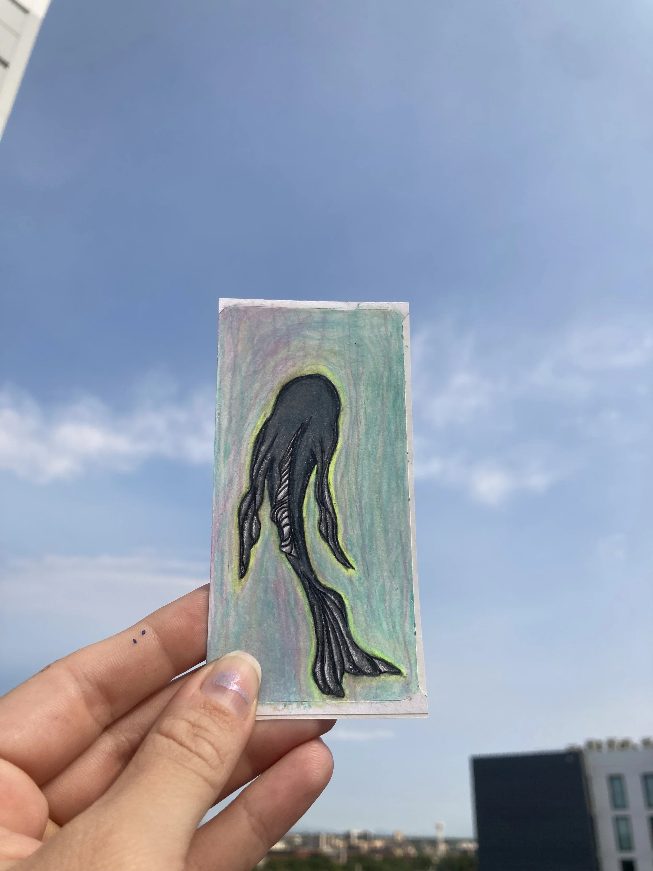 Hand drawn sticker of black fish held up against the sky