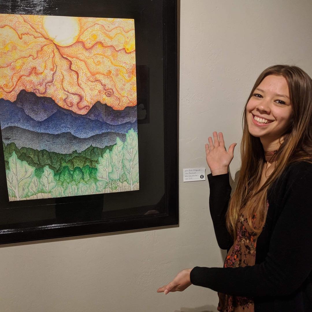 Artist standing by a large framed artwork titled Mountains