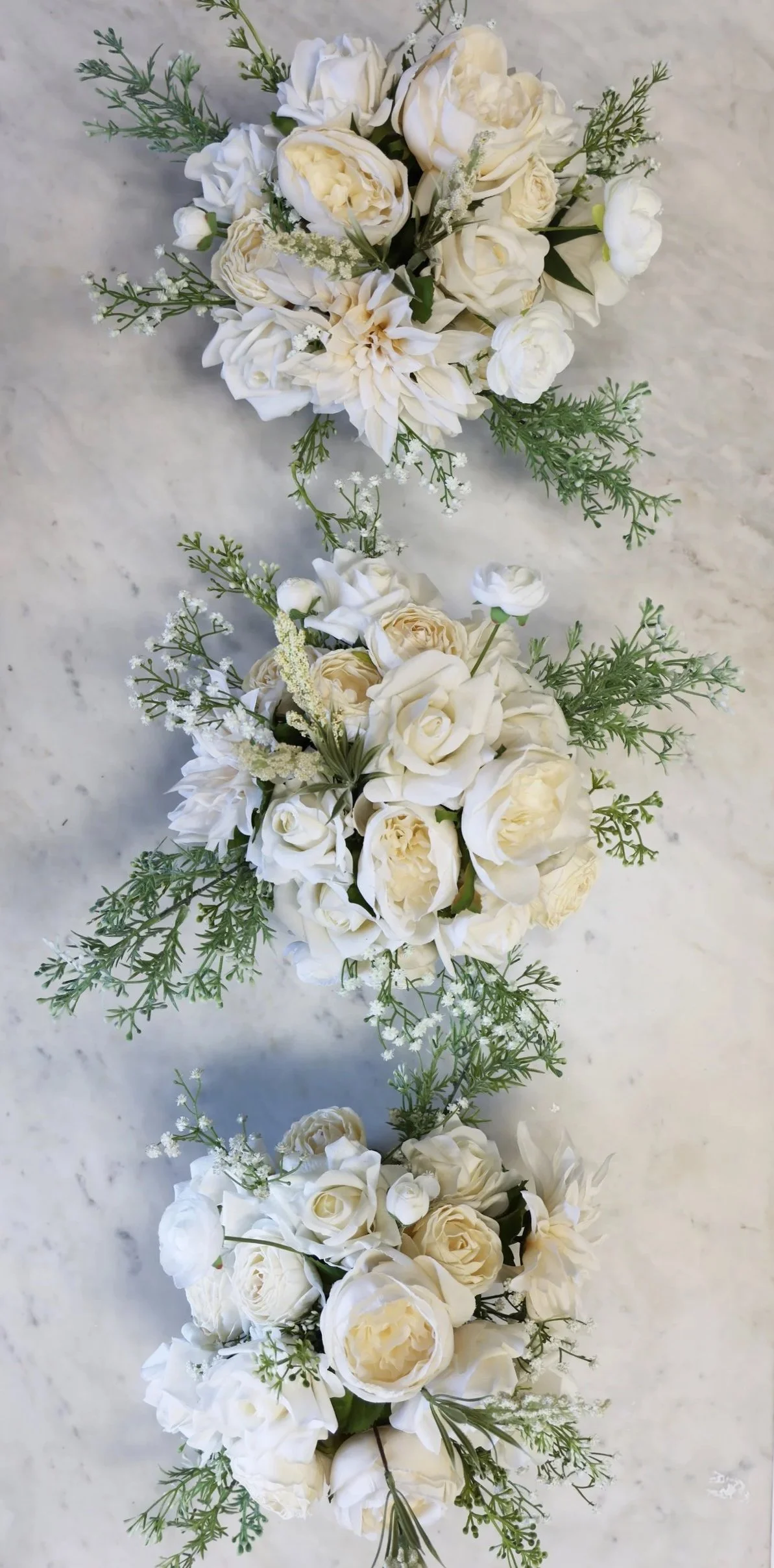 Overhead view of three white rose flower centerpieces on a white marble tabletop.