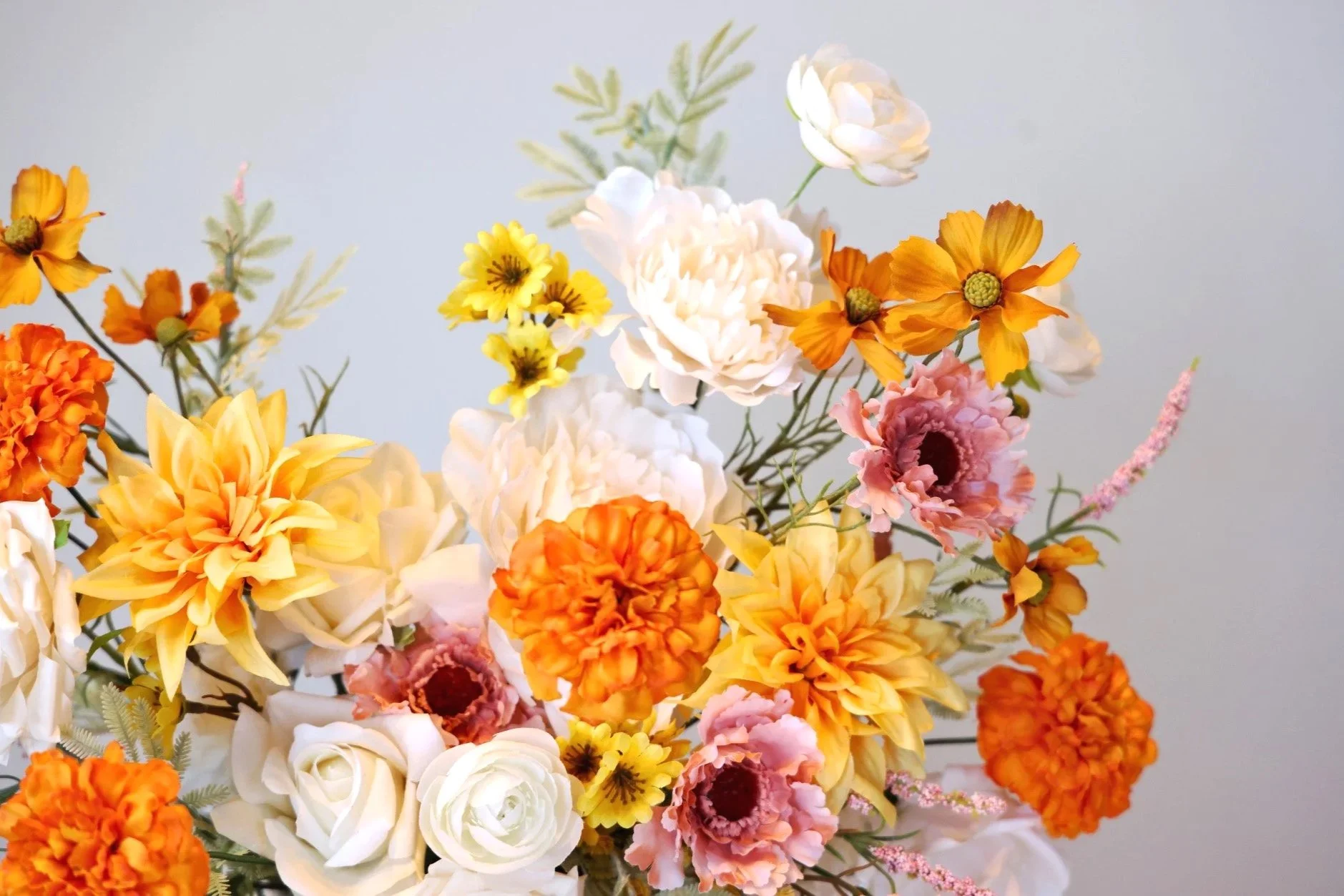 White, yellow, orange, and pink flower arrangement against white wall backdrop