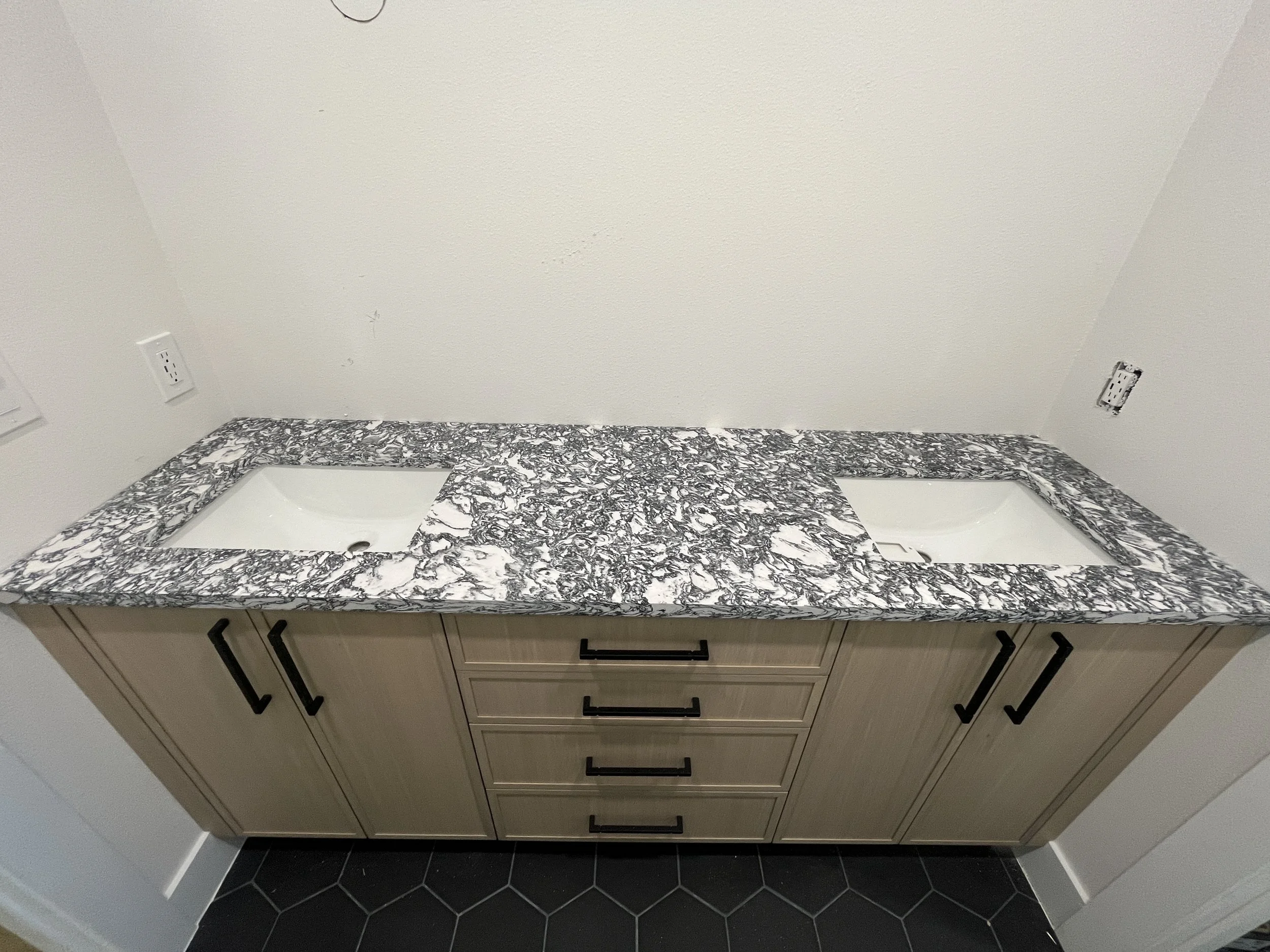 Bathroom vanity with light wood cabinets, black hardware, two sinks with black faucets, large rectangular mirrors, hanging pendant lights, and a wall-mounted light fixture.