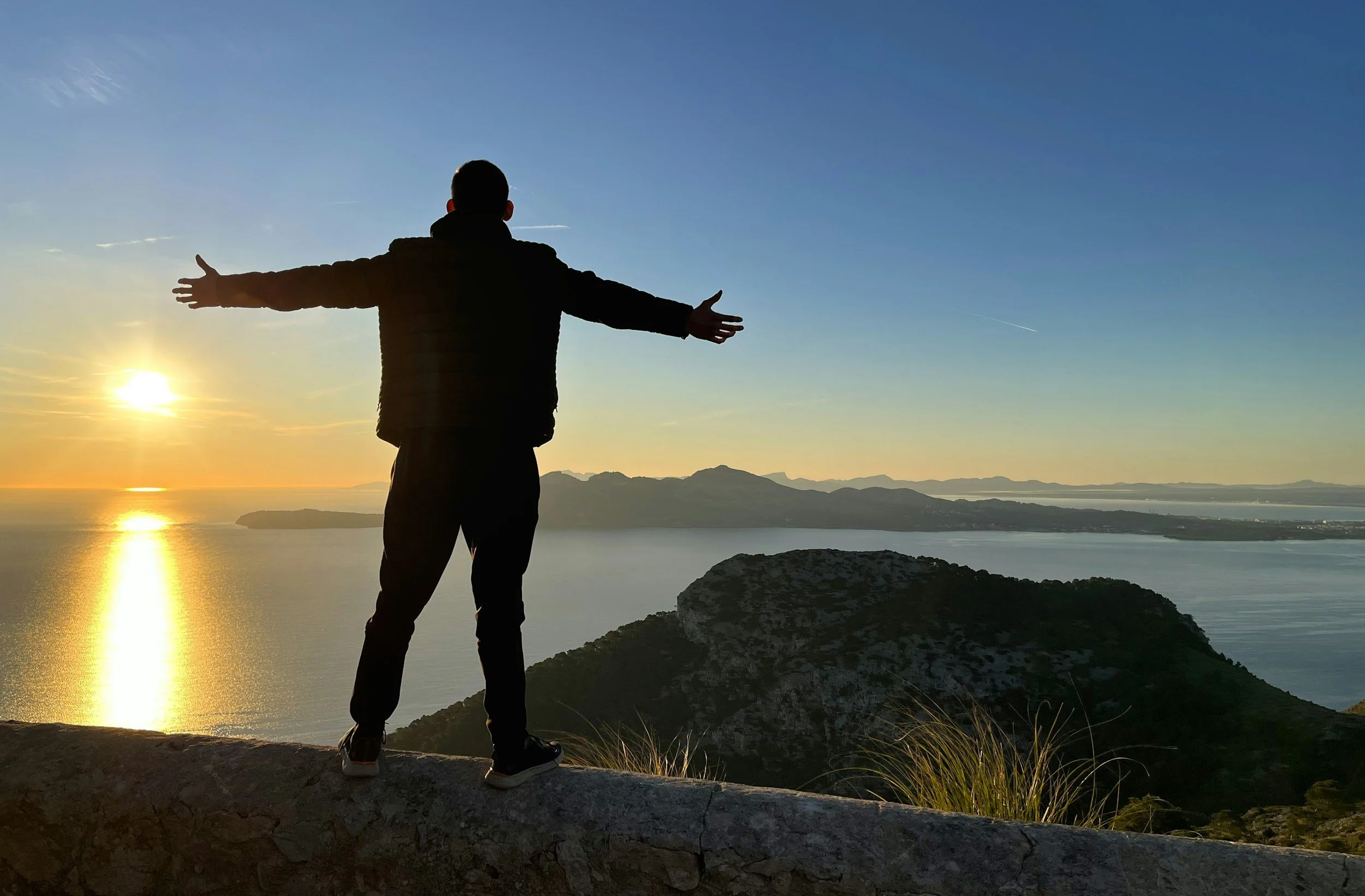 Person standing on a cliff at sunset with arms open, representing values-driven living through ACT therapy in Florida