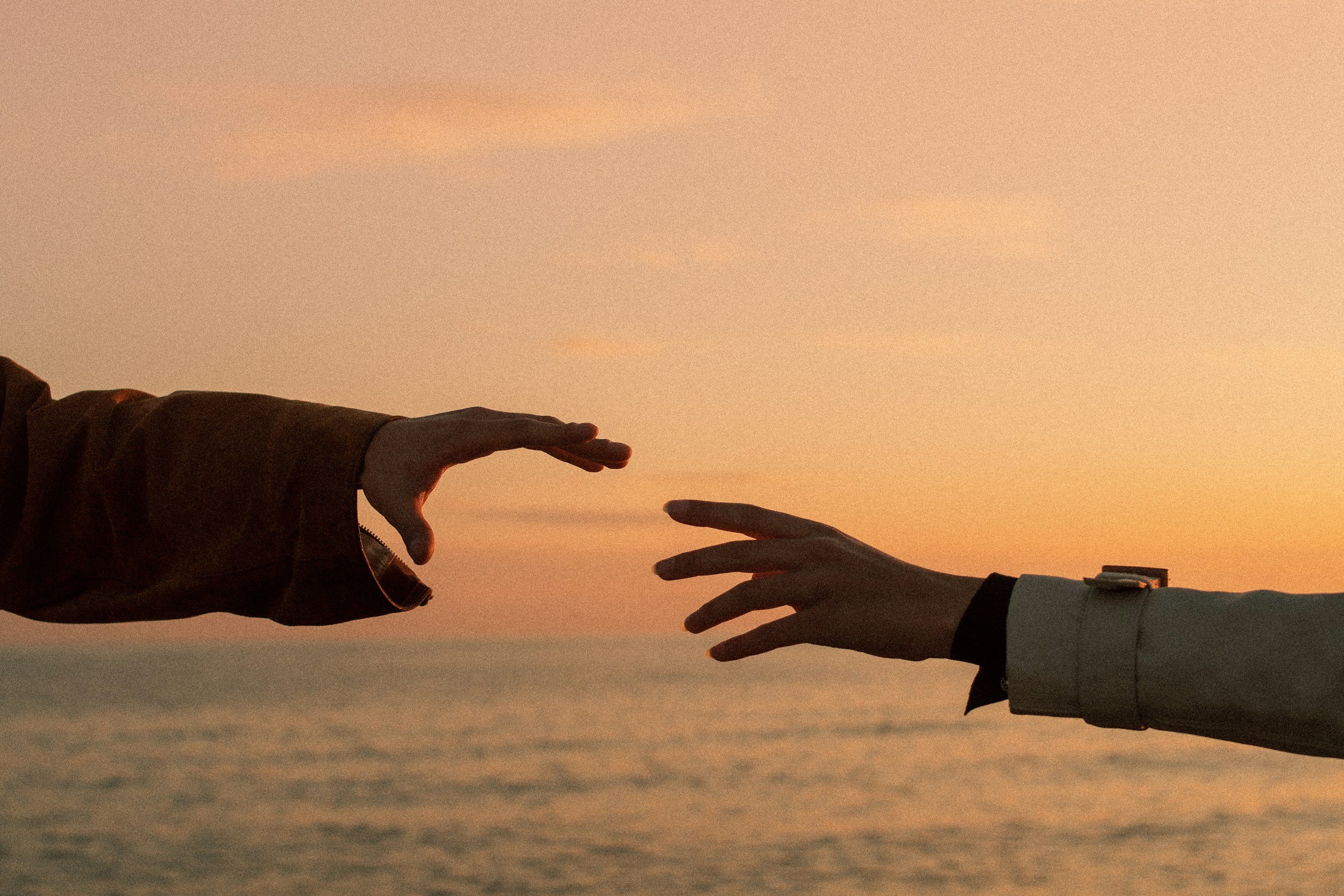 Two hands reaching toward each other at sunset symbolizing grief counseling and emotional support in Tampa and St. Petersburg.
