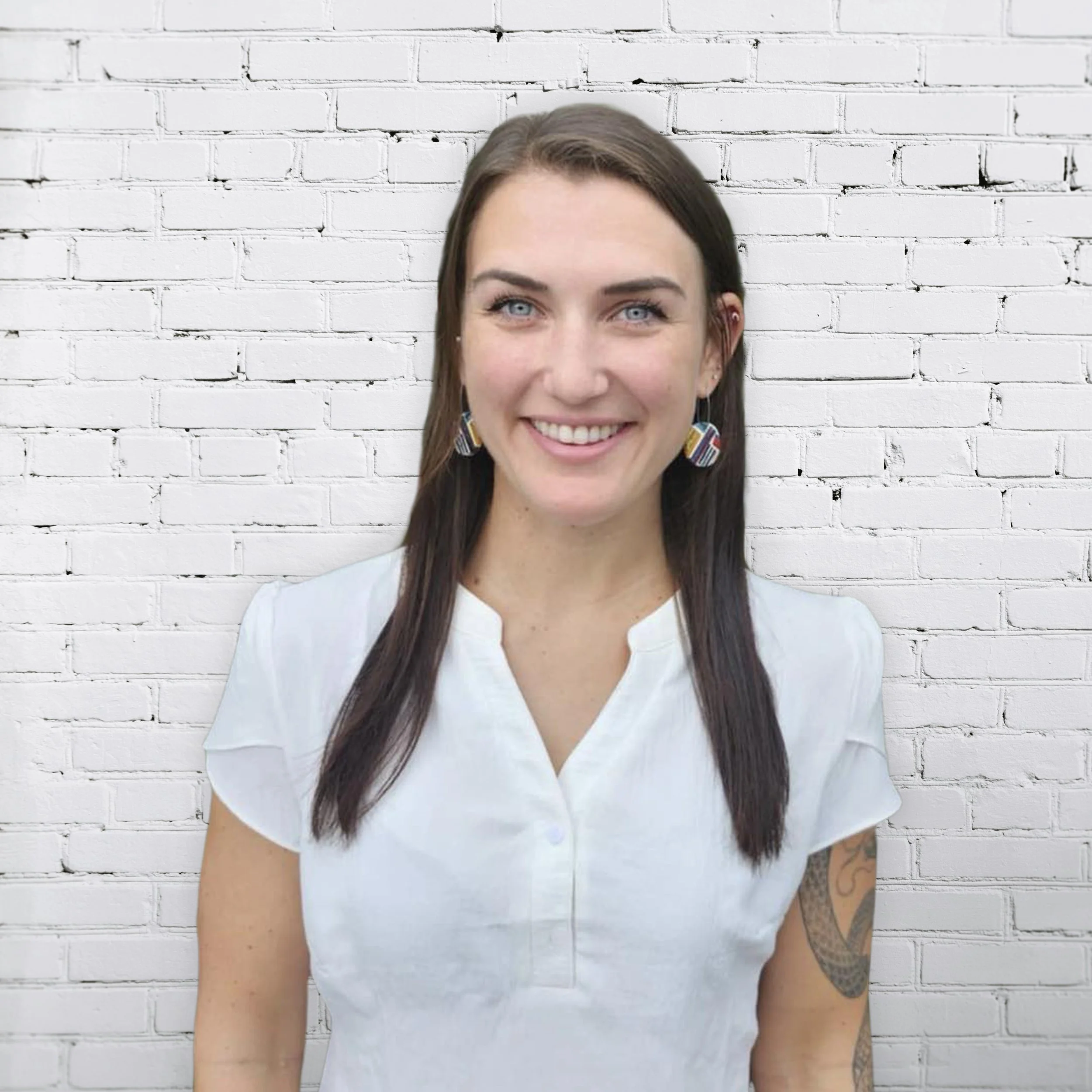 Woman with long brown hair wearing a white shirt, smiling in front of a white brick wall.