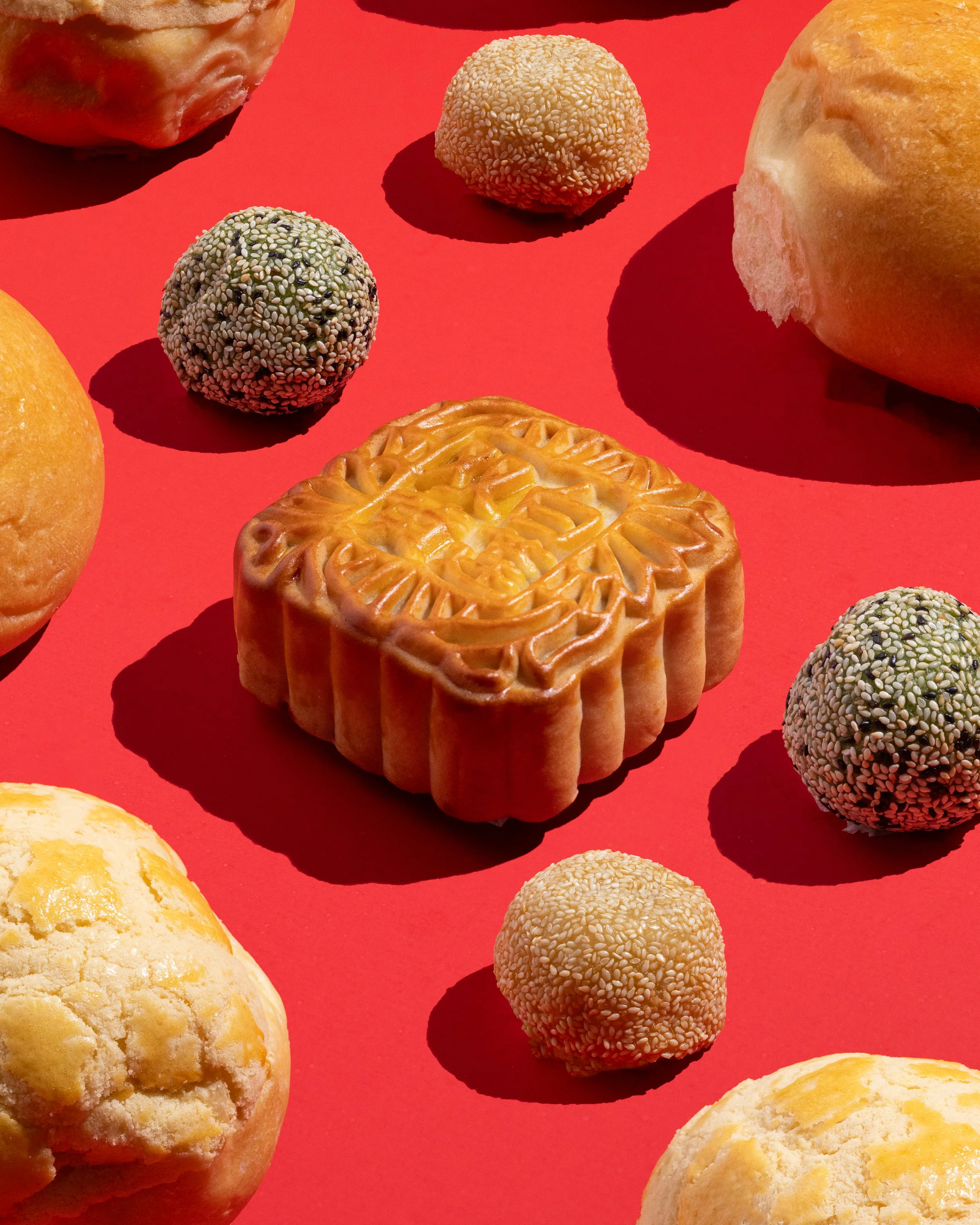 Assorted baked goods from MeeSum Pastry in Seattle including cookies, sesame seed balls, and bread placed on a bright red background.