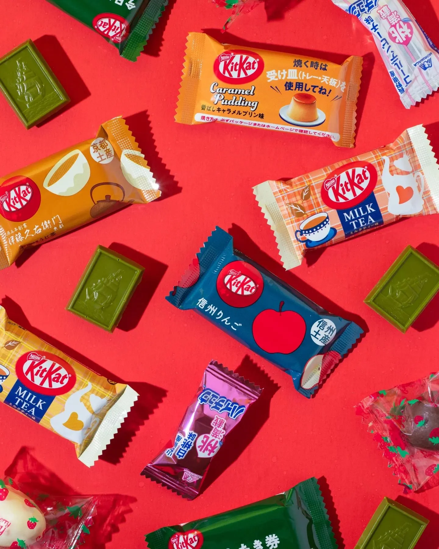 Flatlay of various small Japanese candies and snack packages including Kit Kat flavors, on a red surface.