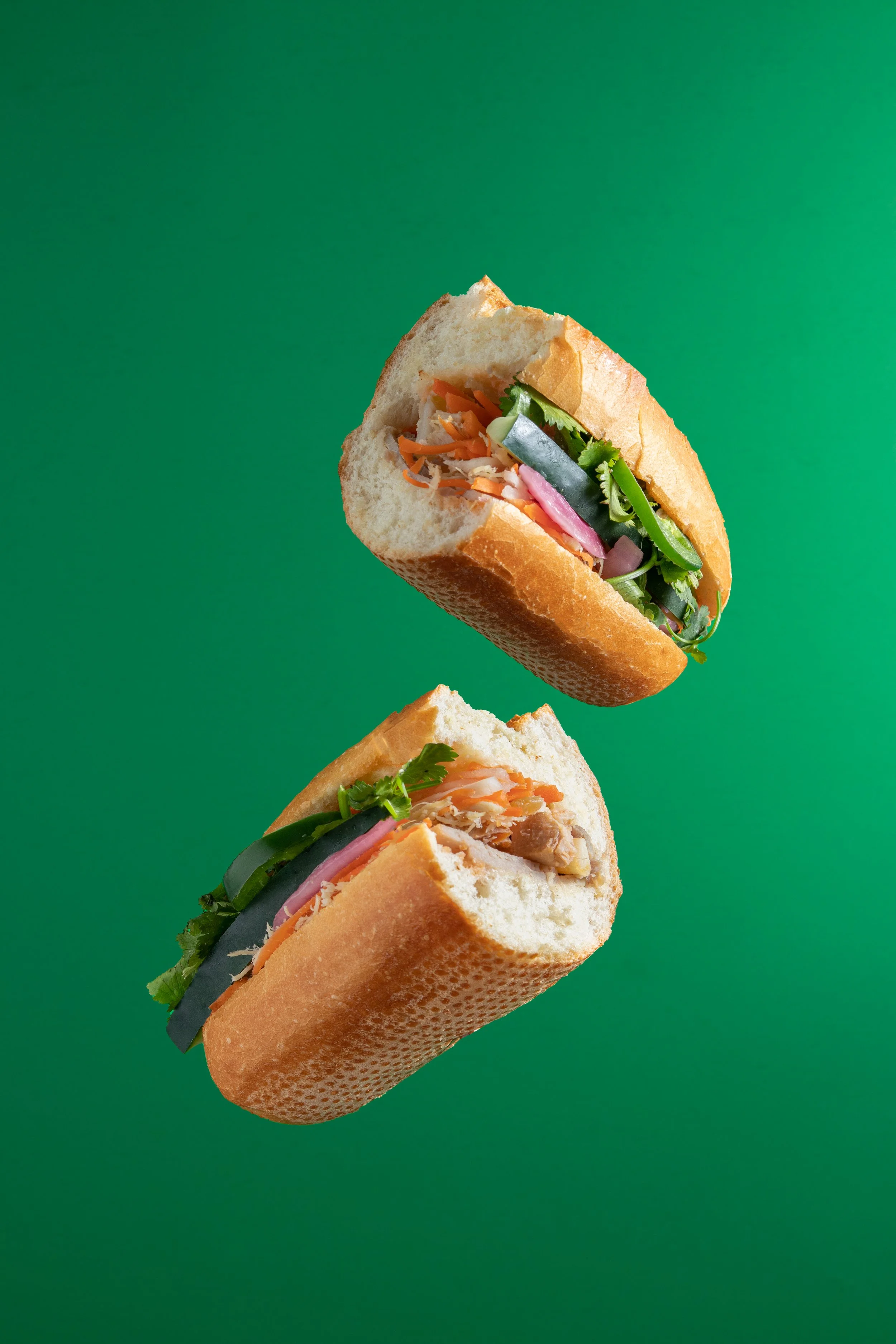 Two Vietnamese bánh mì sandwiches from Cafe 79 in Kirkland with various fresh vegetables and meats against a green background.