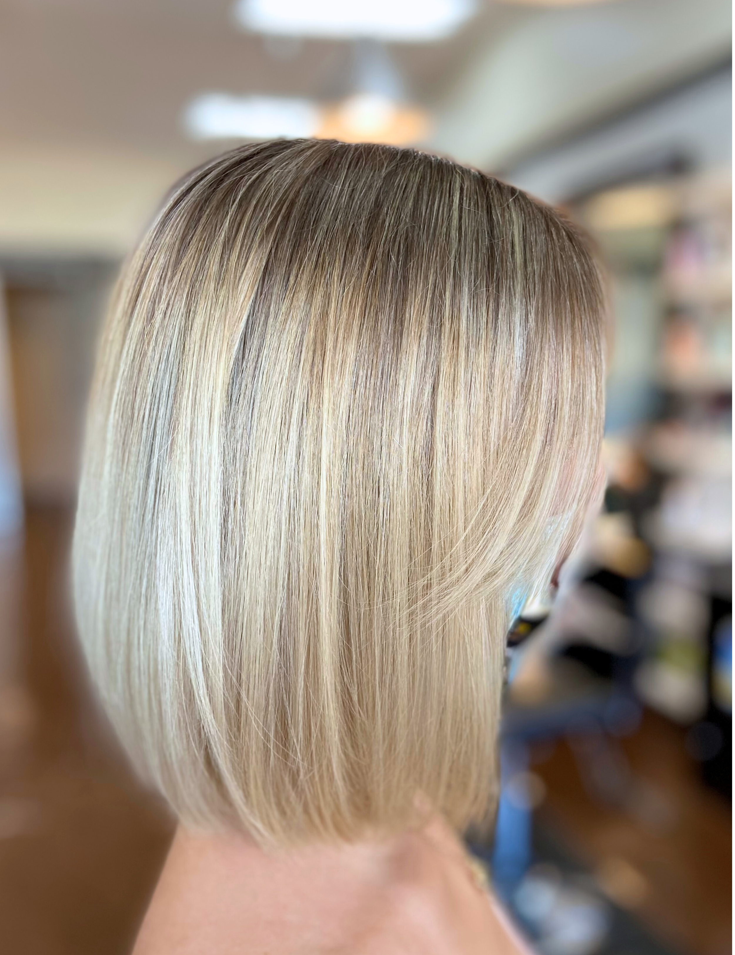 Close-up of a woman's blonde bob haircut with smooth, shiny hair in a salon setting.